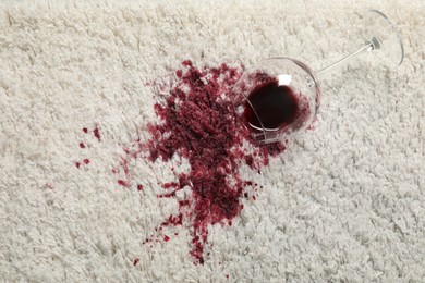 Photo of Overturned glass and spilled red wine on white carpet, top view