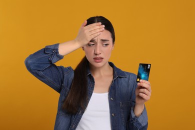 Worried woman with credit card on orange background. Debt problem