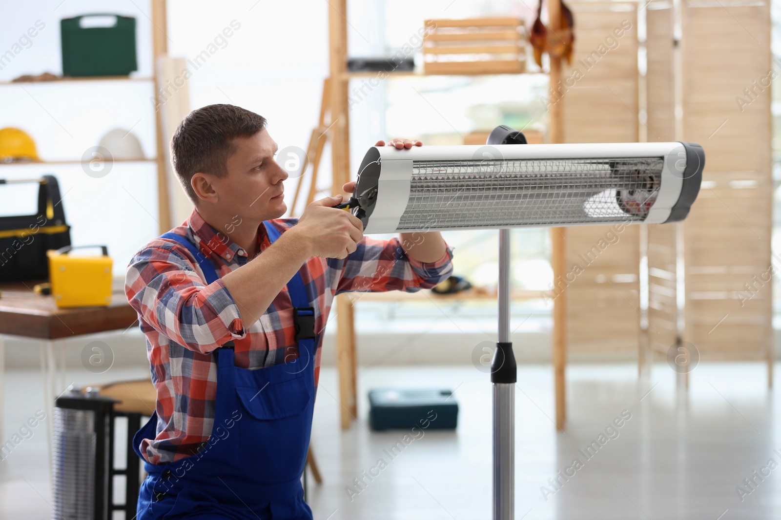 Photo of Professional technician repairing electric infrared heater with pliers indoors