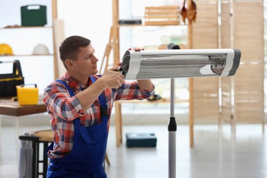 Photo of Professional technician repairing electric infrared heater with pliers indoors