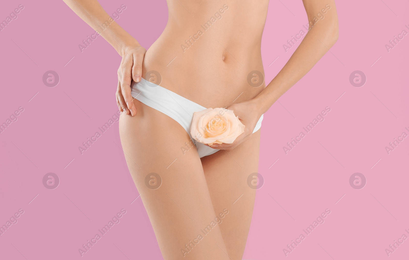 Photo of Woman with flower showing smooth skin after bikini epilation on pink background, closeup. Body care concept