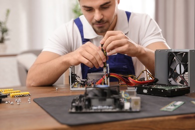 Male technician repairing power supply unit at table indoors