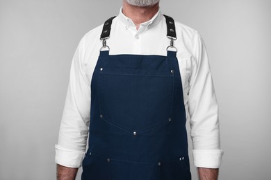 Man wearing kitchen apron on grey background, closeup. Mockup for design