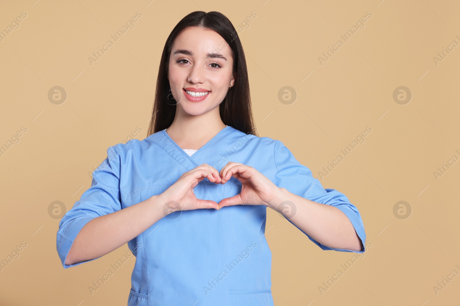 Photo of Nurse in medical uniform making heart with hands on light brown background. Space for text