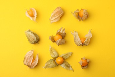 Photo of Ripe physalis fruits with calyxes on yellow background, flat lay