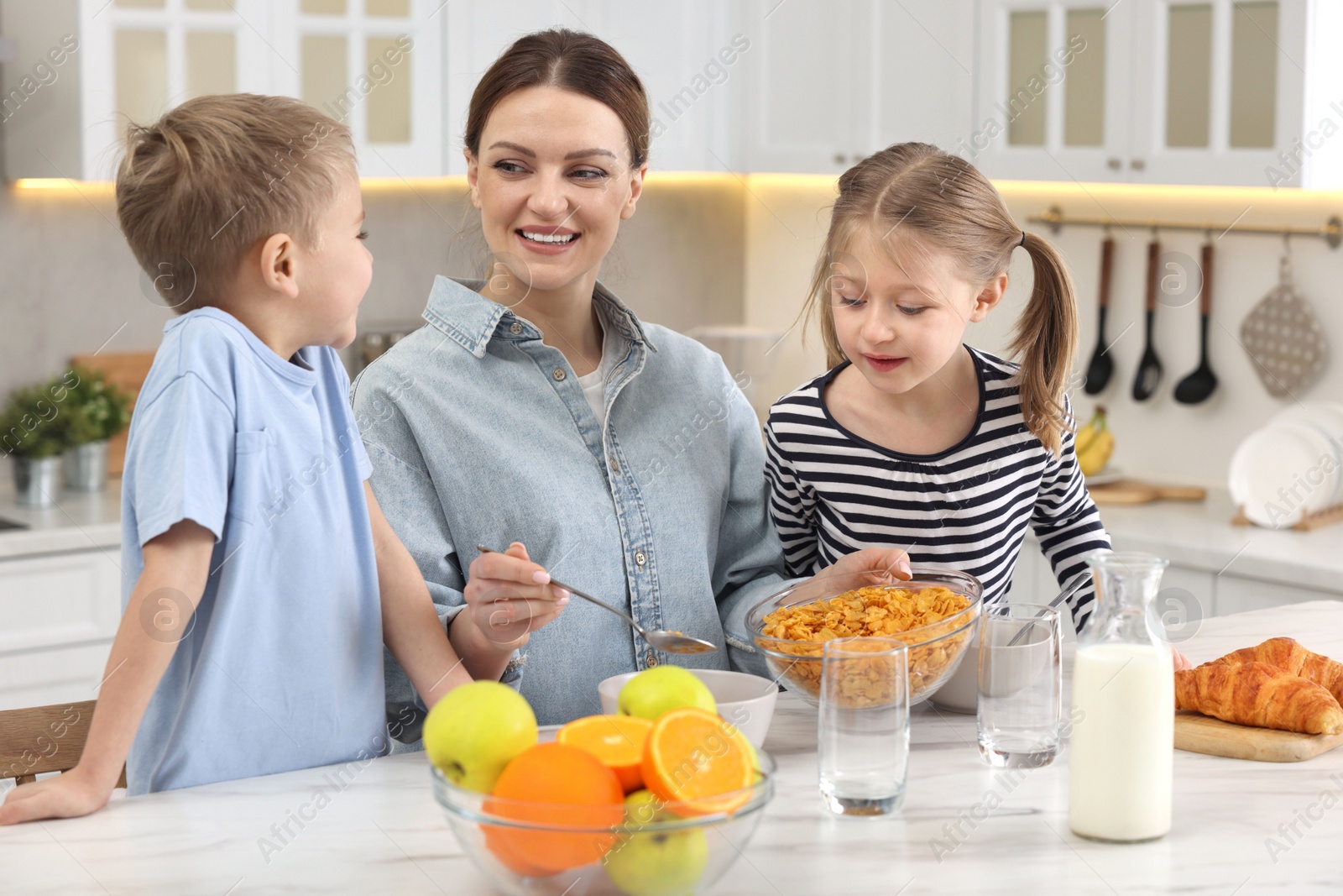 Photo of Mother and her little children having breakfast at table in kitchen