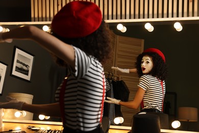 Photo of Young woman in mime costume posing near mirror indoors