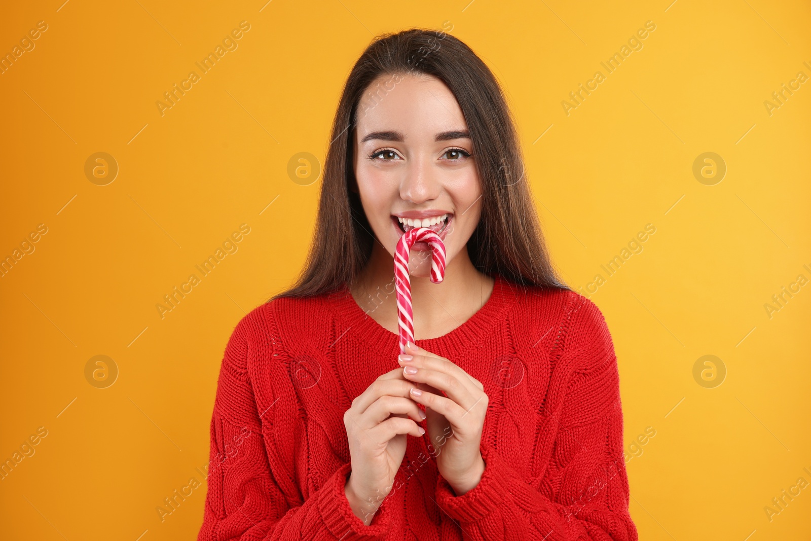 Photo of Young woman in red sweater holding candy cane on yellow background. Celebrating Christmas