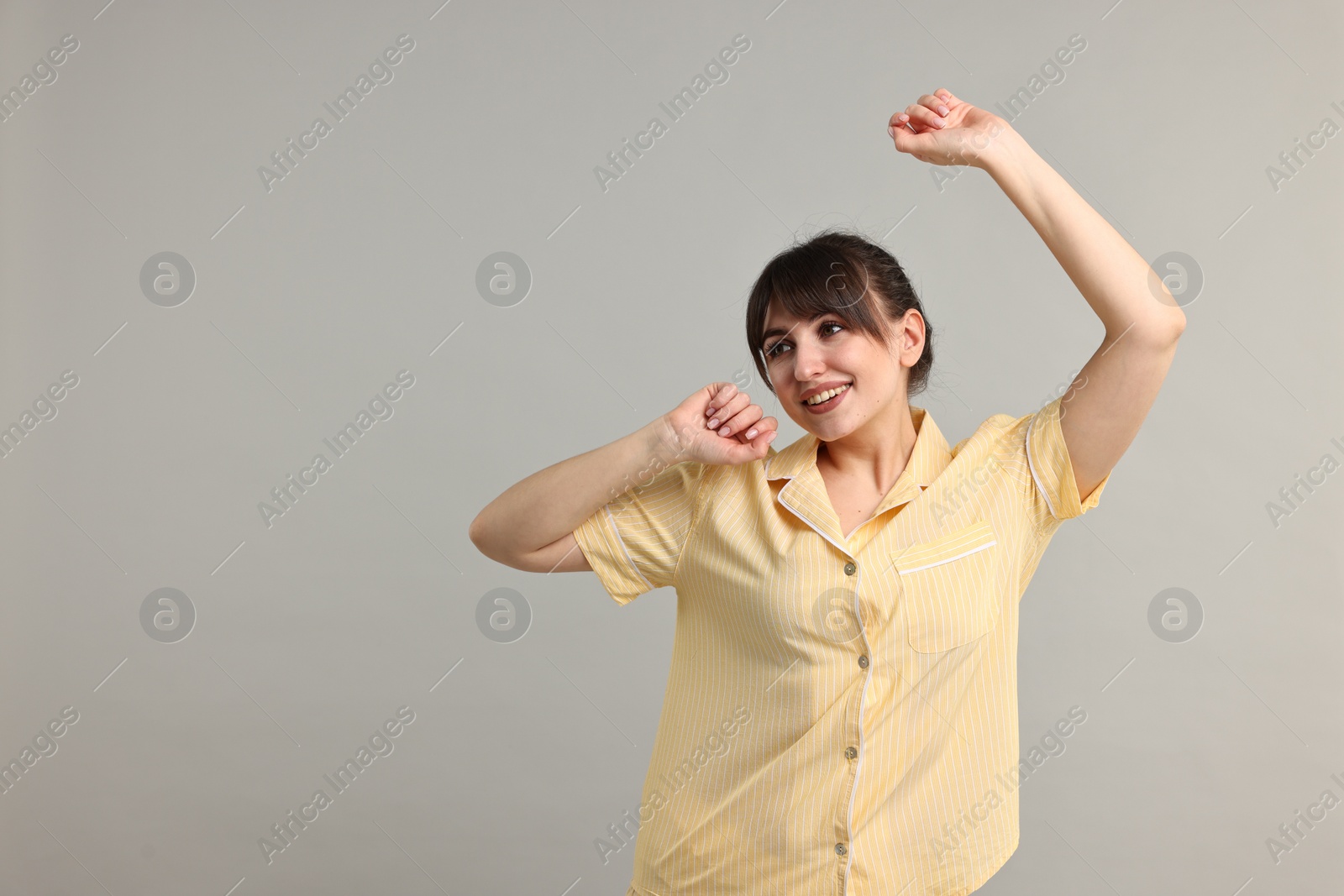 Photo of Woman in pyjama stretching on grey background, space for text