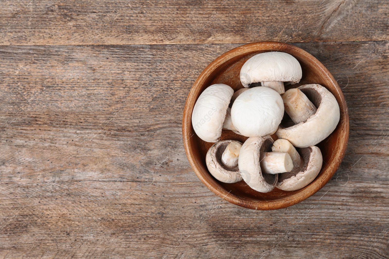 Photo of Bowl of fresh champignon mushrooms on wooden background, top view with space for text