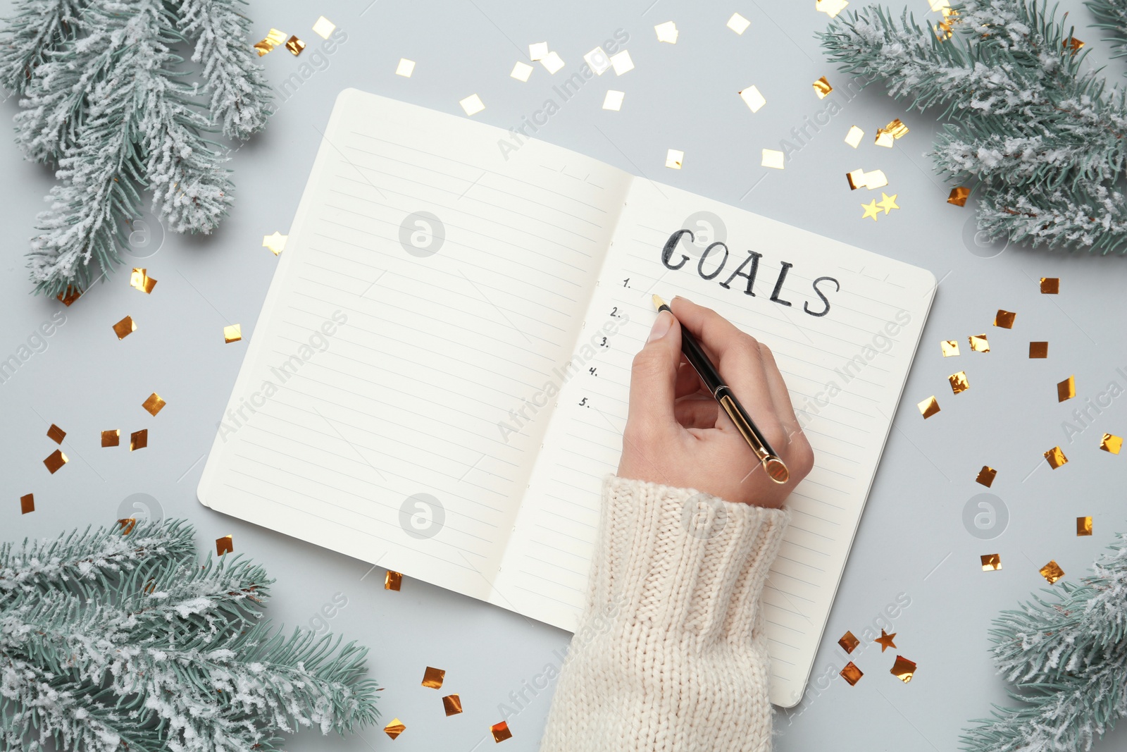 Photo of Woman writing in notebook at light grey table with  Christmas decorations, top view. New aims