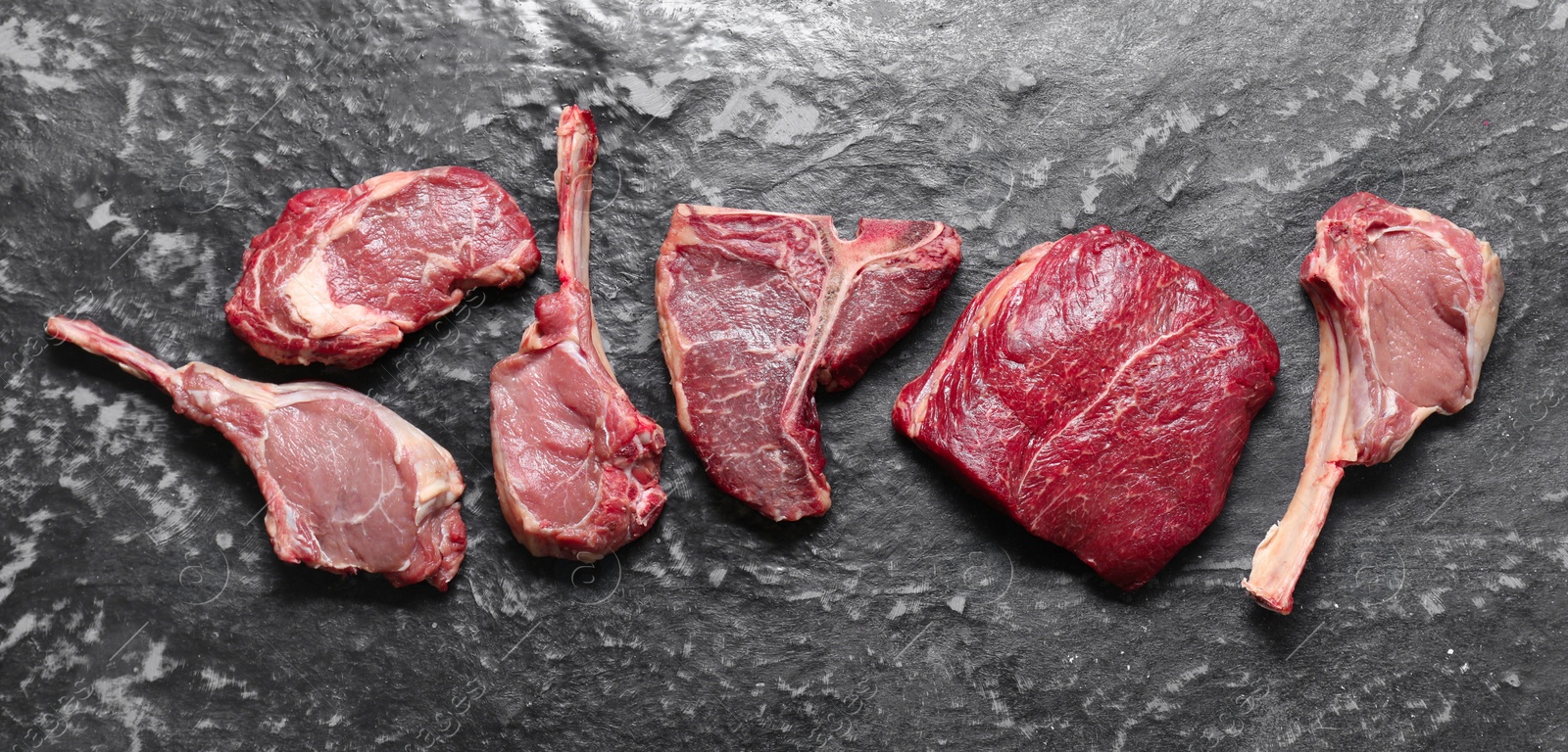 Photo of Fresh raw beef cuts on grey textured table, flat lay