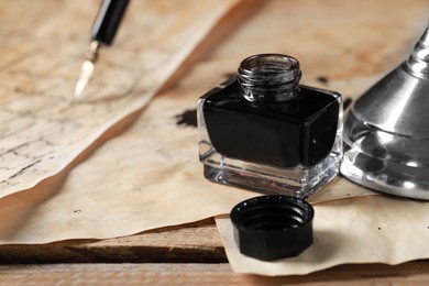 Open inkwell and vintage parchment on wooden table, closeup