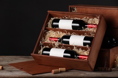 Box with wine bottles on wooden table against black background