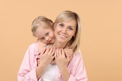 Photo of Daughter hugging her happy mother on beige background