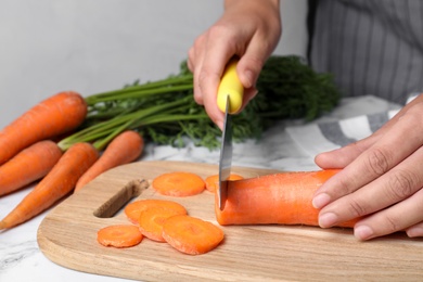 Woman cutting ripe carrot on wooden board at table, closeup