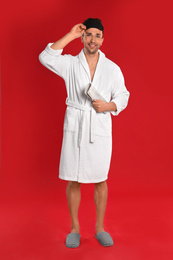 Happy young man in bathrobe with newspaper on red background