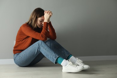 Photo of Sad young woman sitting on floor near grey wall indoors