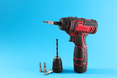 Photo of Modern electric screwdriver and drill bits on light blue background. Space for text