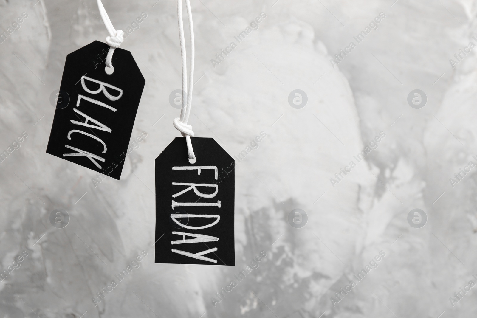 Photo of Tags with words BLACK FRIDAY hanging on light grey background. Space for text