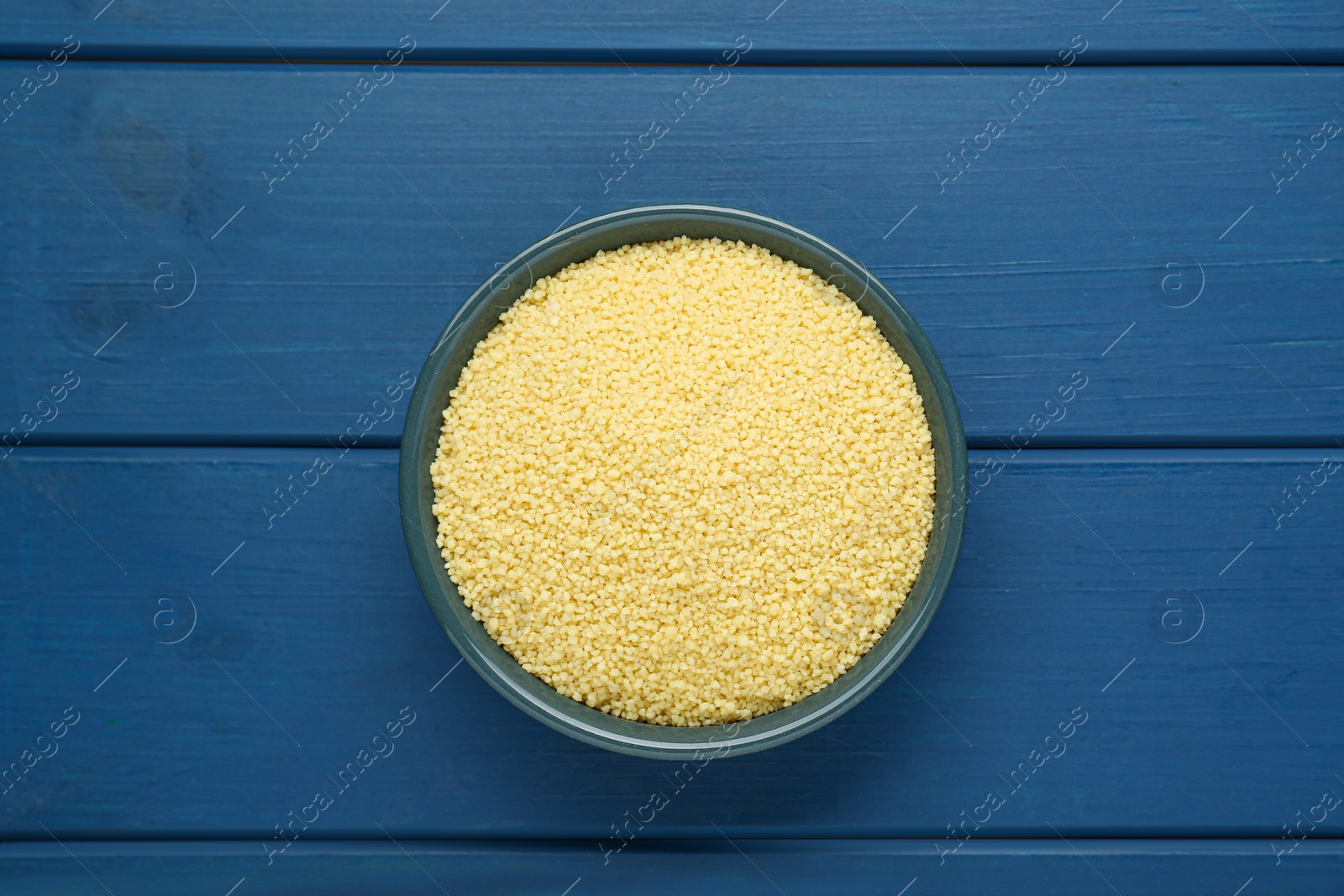 Photo of Bowl of raw couscous on blue wooden table, top view