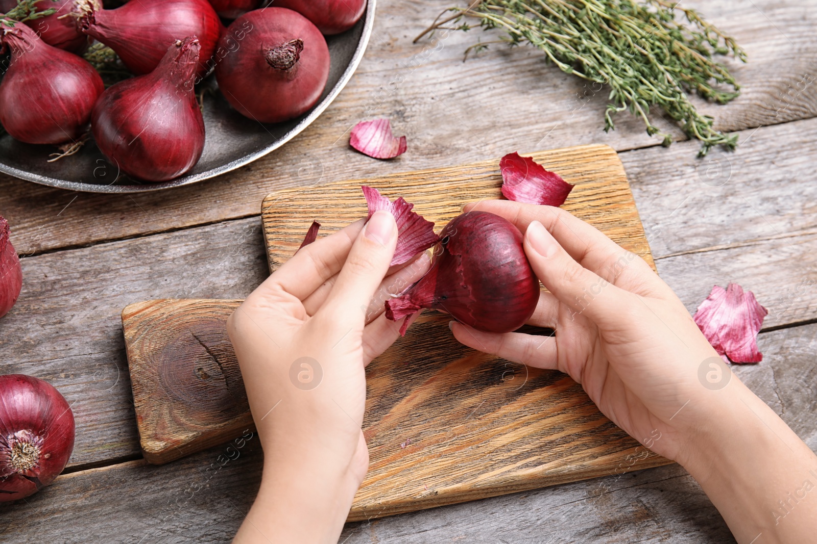 Photo of Woman peeling ripe red onion on wooden table