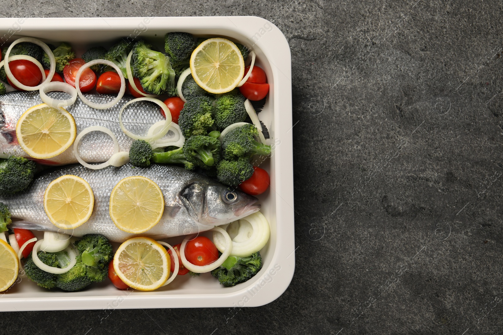 Photo of Raw fish with vegetables and lemon in baking dish on grey textured table, top view. Space for text