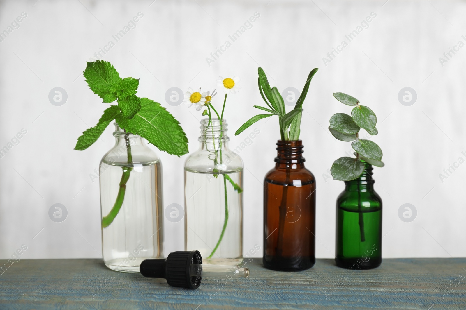 Photo of Glass bottles of different essential oils with plants on table