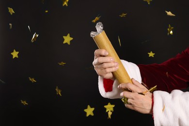 Photo of Man in Santa Claus costume blowing up party popper on black background, closeup