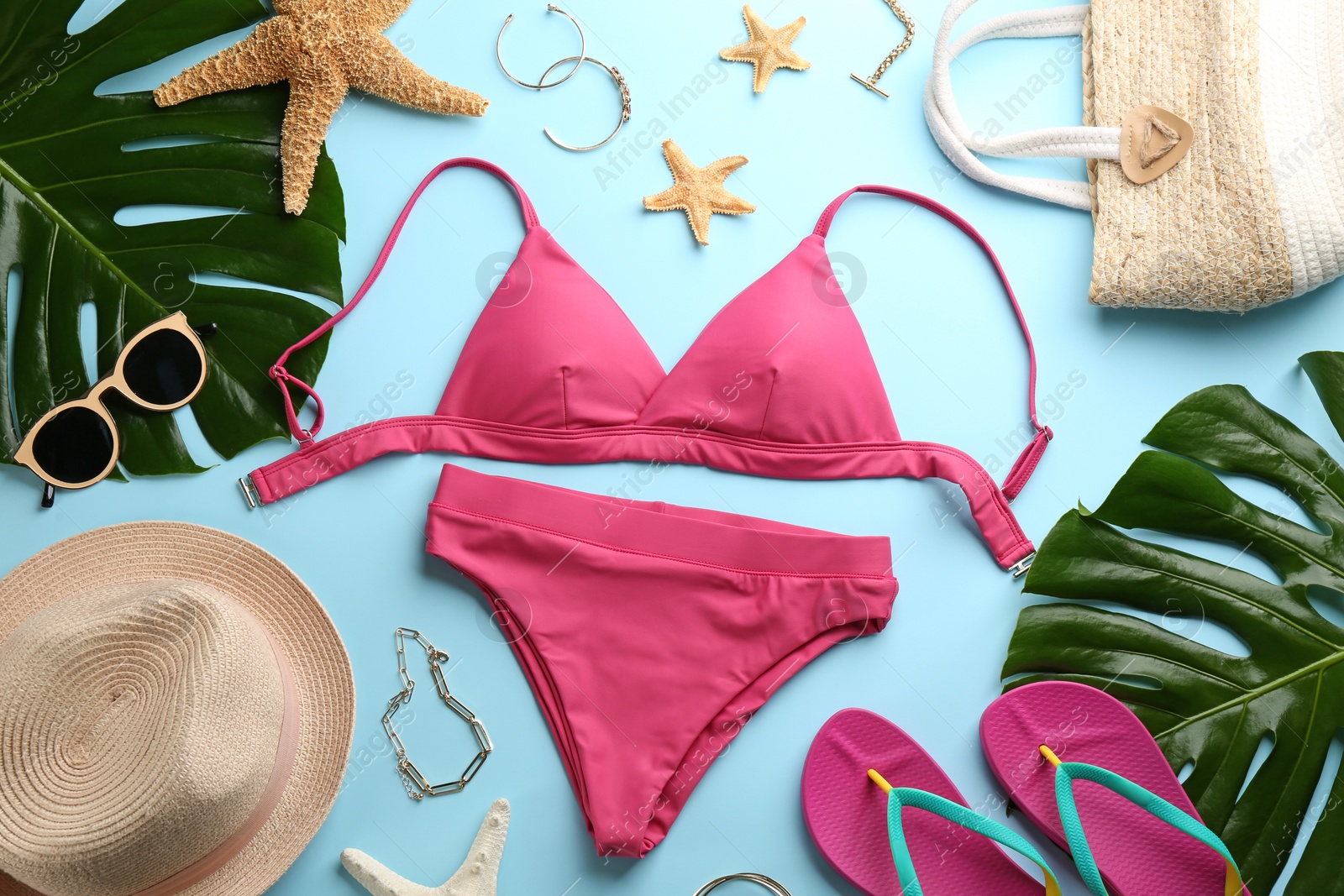 Photo of Beautiful pink bikini and beach accessories on light blue background, flat lay