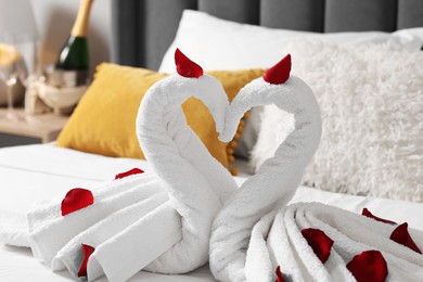 Honeymoon. Swans made with towels and beautiful rose petals on bed, closeup