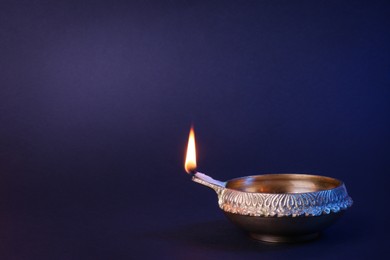Lit diya lamp on purple background, space for text. Diwali celebration