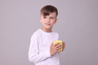 Photo of Cute boy with yellow ceramic mug on light grey background