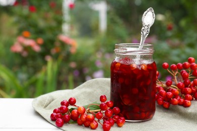Photo of Jar of tasty jam and viburnum berries on table outdoors, space for text