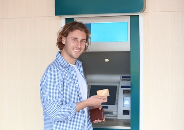 Photo of Young man with credit card near cash machine outdoors