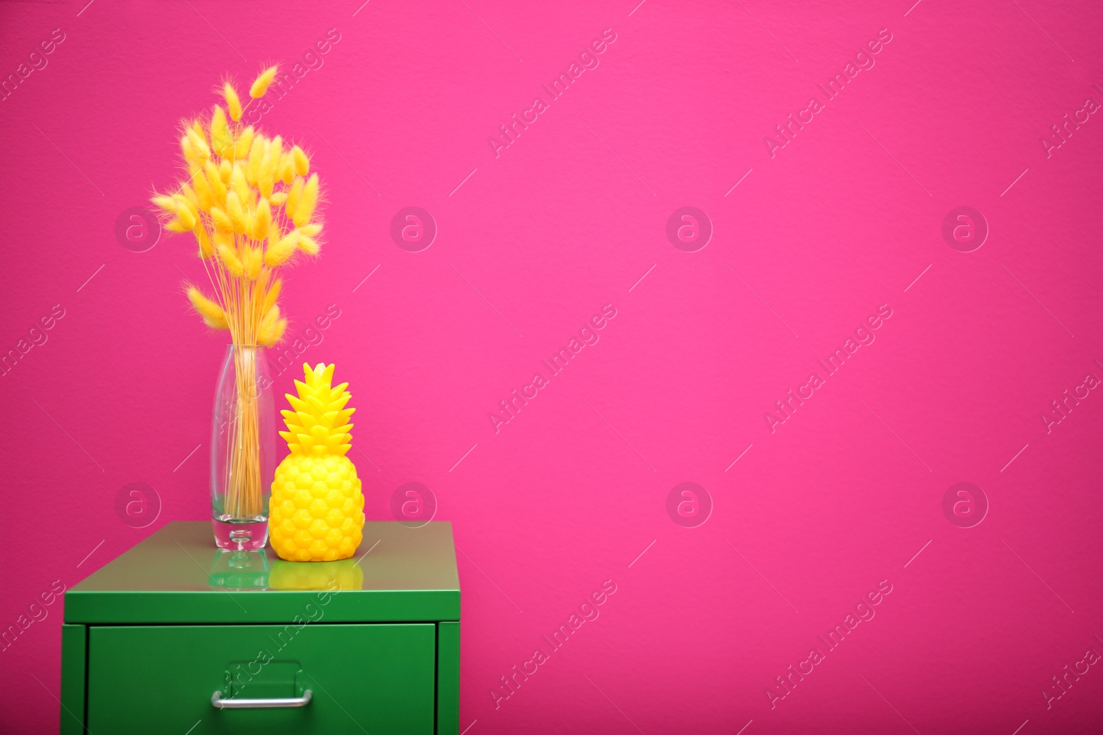 Photo of Stylish pineapple candle on drawer unit against color background. Home decorating idea