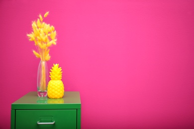 Stylish pineapple candle on drawer unit against color background. Home decorating idea