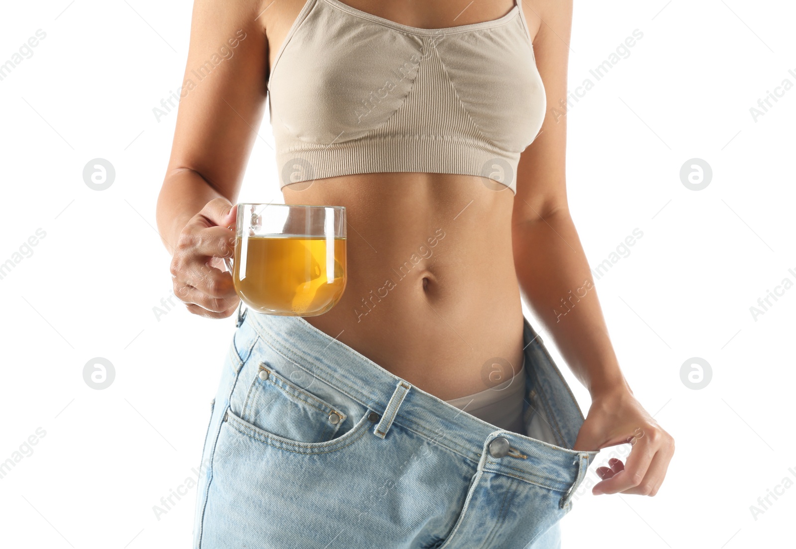 Photo of Young woman in old big jeans with cup of tea showing her diet results on white background, closeup