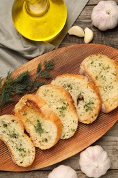 Photo of Tasty baguette with garlic, dill and oil on wooden table, flat lay