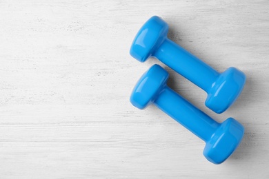 Photo of Bright dumbbells and space for text on wooden background, flat lay. Home fitness