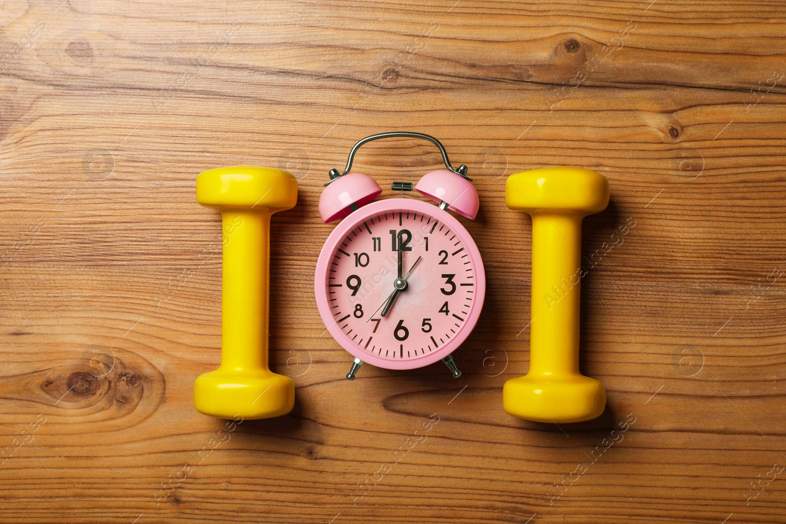 Photo of Alarm clock and dumbbells on wooden table, flat lay. Morning exercise