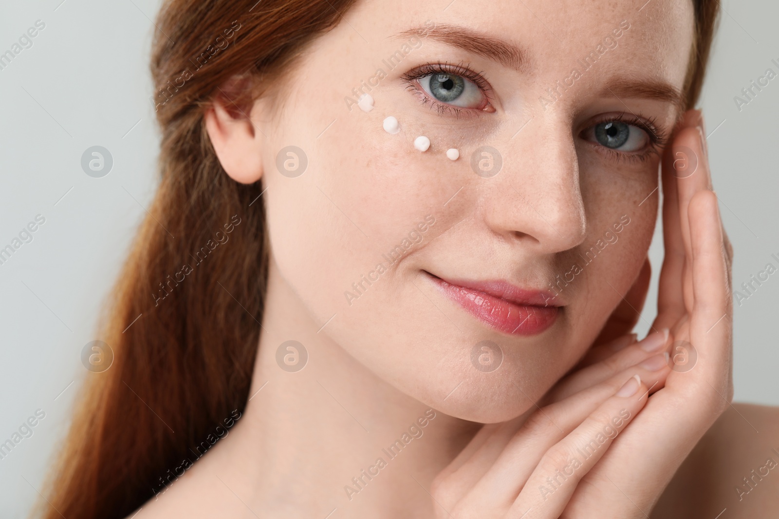 Photo of Beautiful woman with freckles and cream on her face against grey background, closeup