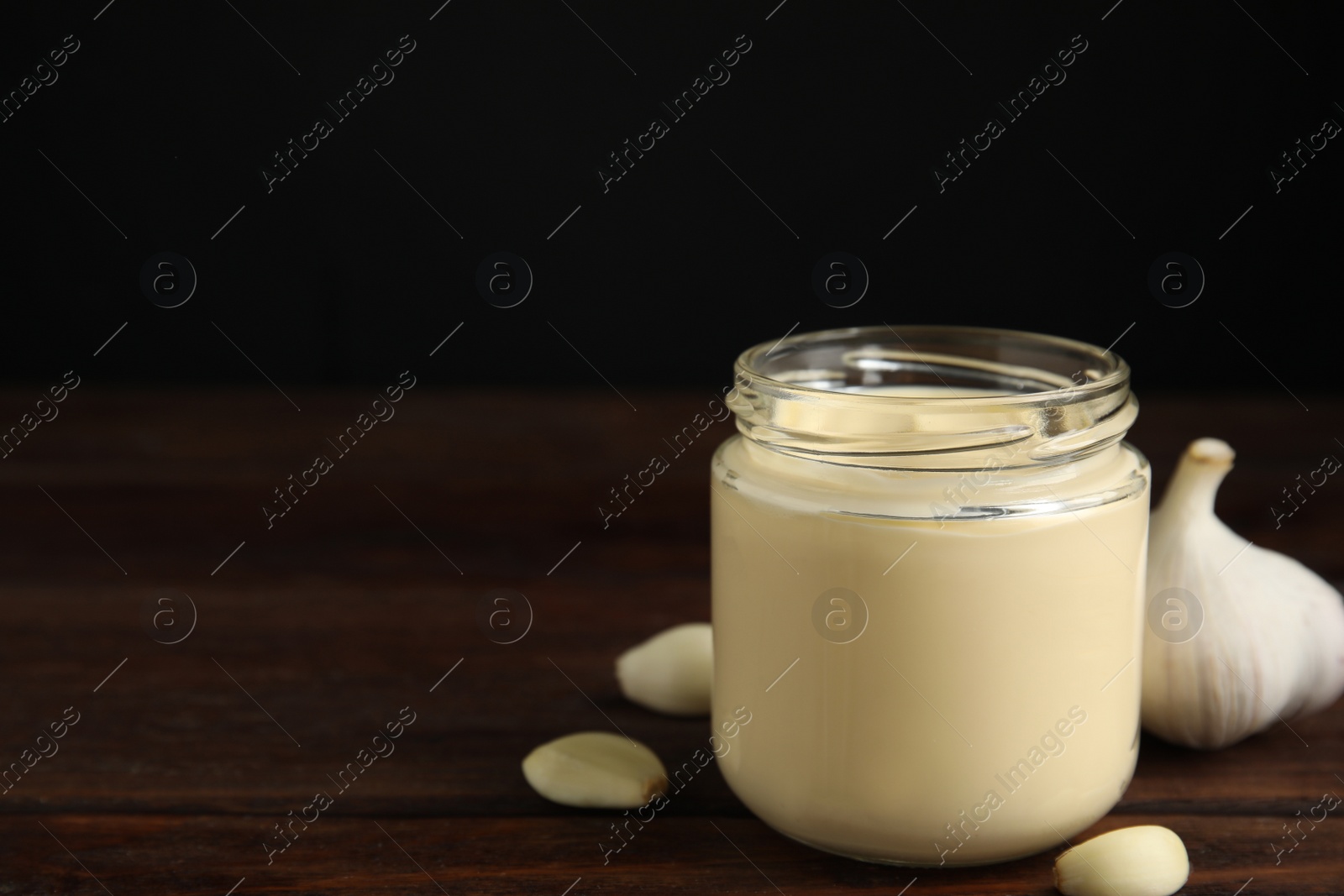 Photo of Jar of delicious mayonnaise and fresh garlic on wooden table. Space for text
