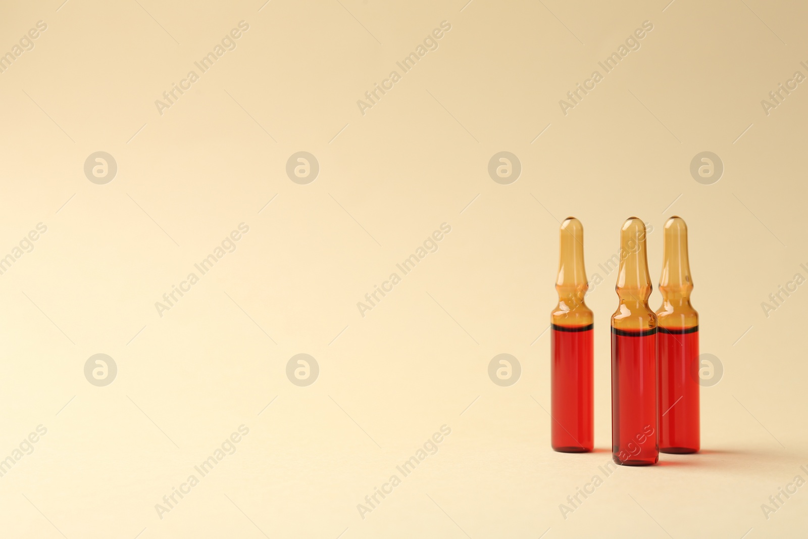 Photo of Glass ampoules with liquid on beige background. Space for text