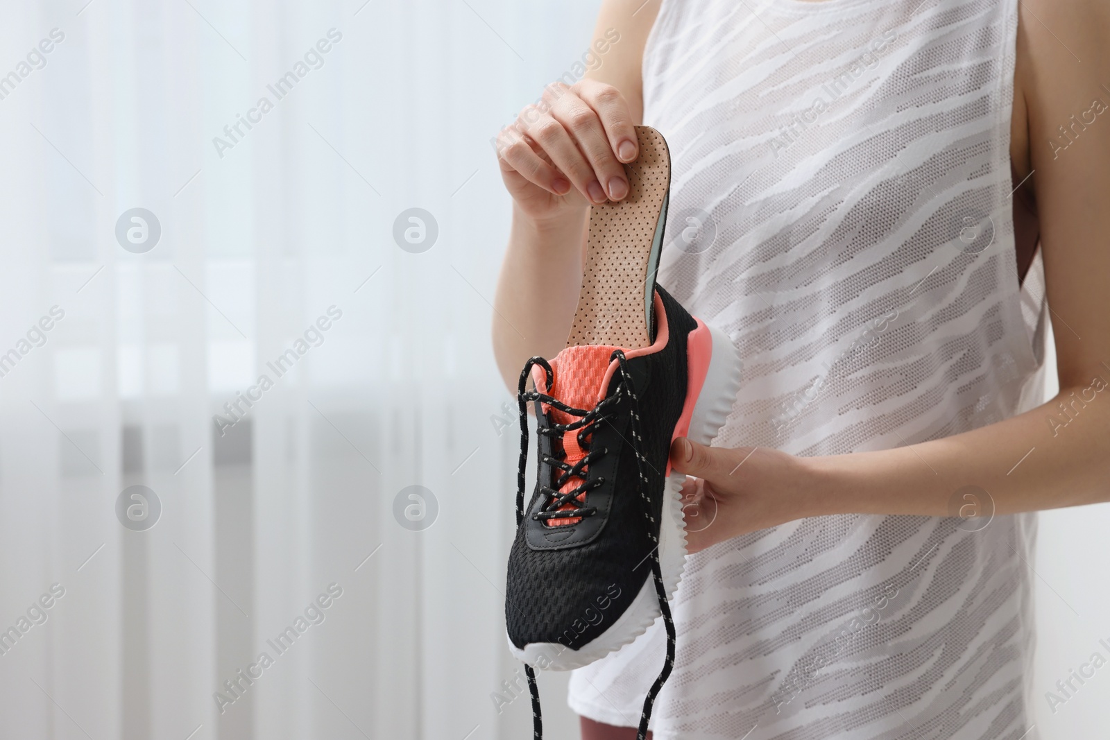 Photo of Woman putting orthopedic insole into shoe indoors, closeup. Foot care