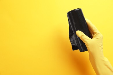 Photo of Janitor in rubber glove holding roll of black garbage bags over yellow background, top view. Space for text