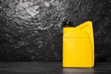 Photo of Motor oil in yellow canister on black table near dark wall, space for text