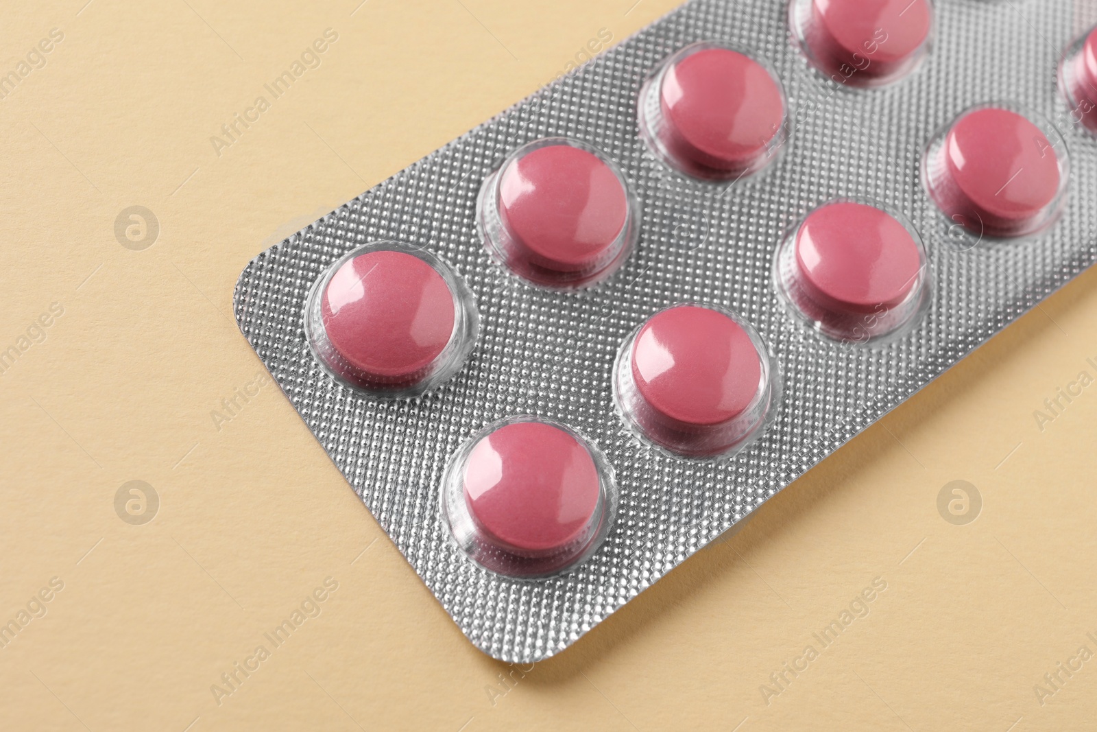 Photo of Pink pills in blister on beige background, closeup