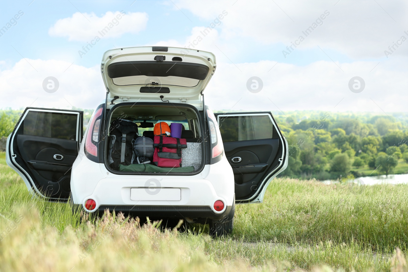 Photo of Car with camping equipment in trunk on green field. Space for text