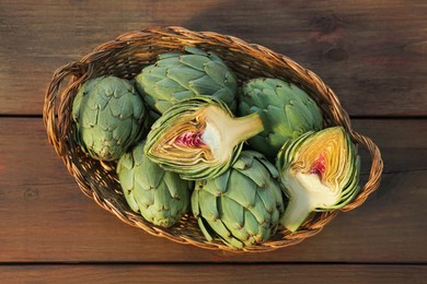 Photo of Wicker basket with fresh raw artichokes on wooden table, top view